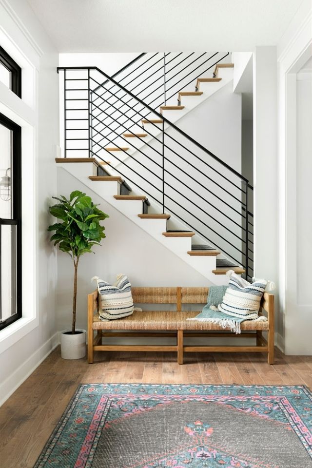 Entryway into home with black staircase and fiddle leaf fig tree and bench
